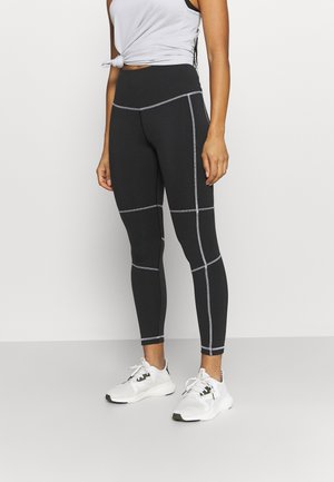 Sorte leggings med kontrastfarvet grå syning og en høj talje, parret med en lysegrå ærmeløs top og hvide sportssko.