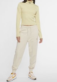 Gul ribbad höghalstopp med scalloperade kanter, kombinerad med lösa beige joggers med elastisk midja och logodetalj. Vita och orange sneakers.