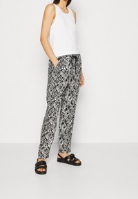 Svartvitt mönstrade byxor i ett lätt material, med en avslappnad passform och sidofickor, kombinerat med en vit ärmlös topp och svarta sandaler.