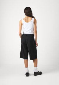 Czarne szorty culotte wykonane z lekkiego materiału, o klasycznym kroju i pojedynczej tylnej kieszeni, zestawione z białym topem na ramiączkach i czarnymi butami.