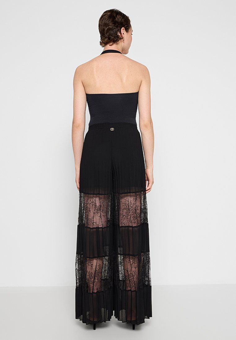 Jupe maxi plissée noire avec des panneaux en dentelle transparente et une taille structurée. Comprend un haut à halter, mettant en valeur des couches accentuées et des détails en dentelle complexes.