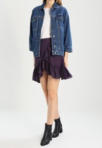 Veste en denim, t-shirt blanc, jupe violette à volants avec motif floral et bottes noires à la cheville. Tenue décontractée en couches.