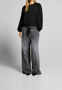 Felpa nera con scollatura rotonda e spalle scese, abbinata a pantaloni grigi a gamba larga con elastico in vita e tasche laterali.
