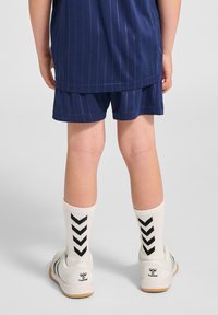 Granatowy sportowy strój w paski z szortami, białe skarpetki z czarnym wzorem w zygzak oraz białe sneakersy z logo i gumową podeszwą.