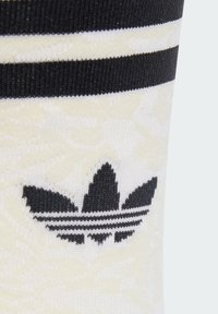 Biele a čierne pruhované ponožky s textúrovaným vzorom a čiernym logom Adidas so symbolom troch listov v oblasti členka.