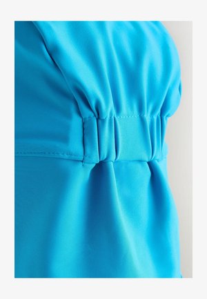 Modra sintetična tkanina z nabrano podrobnostjo na šivu. Gladek tekstura; ima rahlo sijočnost in izrazito šivanje na nabrankah.