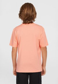 Camiseta de manga corta en tela de durazno claro, con cuello redondo y un diseño liso en la parte posterior. El material parece suave y liso.