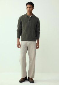 Zielony sweter z prążkowanego dzianiny z kołnierzykiem i trzema guzikami, zestawiony z beżowymi spodnie o szerokich nogawkach i brązowymi wiązanymi butami.