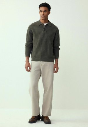 Pulover verde din tricot cu aspect striat, cu guler și trei nasturi, asortat cu pantaloni bej cu croială largă și cizme maro cu șireturi.