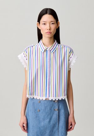 Mujer con una camisa de manga corta a rayas con botones y ribete de encaje, y una falda vaquera azul de talle alto con botones decorativos.
