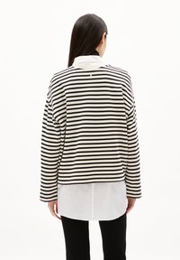 Maglietta a maniche lunghe a righe bianche e nere, sovrapposta a una camicia bianca, con scollatura rotonda e un fit leggermente cropped.