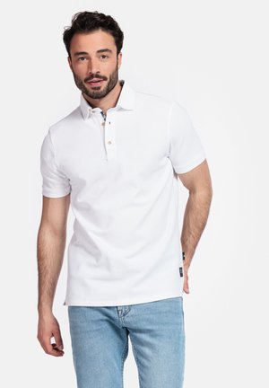 Witte polo met een zachte textuur, een twee-knopen knoopsluiting en een subtiel blauw patroon aan de binnenkant van de kraag. Gecombineerd met lichtblauwe jeans.