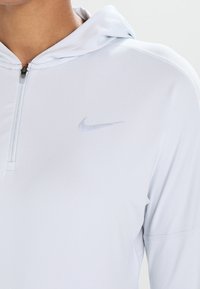 Felpa atletica azzurra con zip a metà, caratterizzata da un discreto logo Nike e un tessuto liscio e textured.