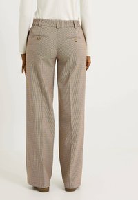 Pantalones de pierna ancha a cuadros en beige, con bolsillos traseros visibles y cintura elástica. Acabados con sutiles líneas multicolores.