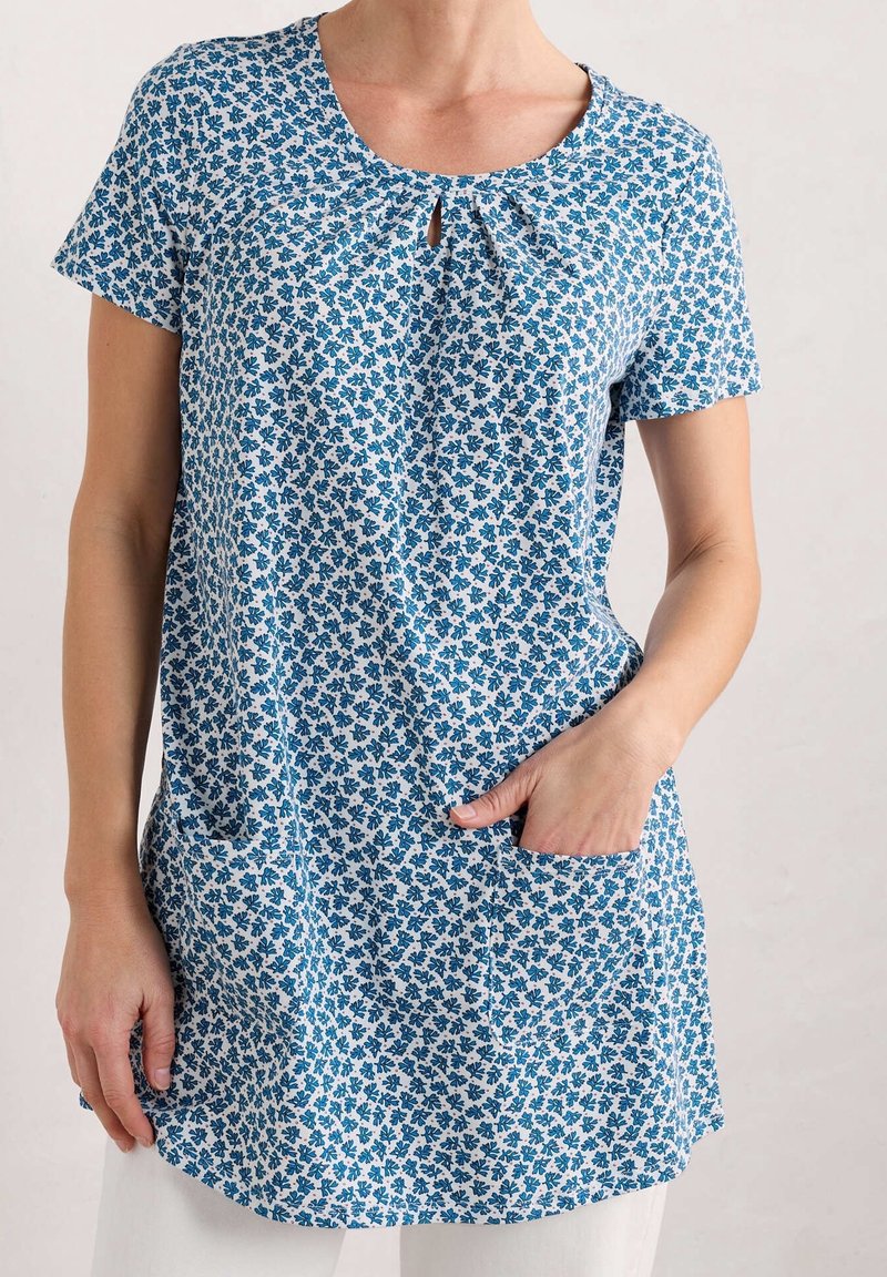 Lyhythihainen sinivalkoinen tunika, jossa on kukkakuvio, avonainen kaula-aukko ja sivutasku. Pehmeä kangas ja rento leikkaus.