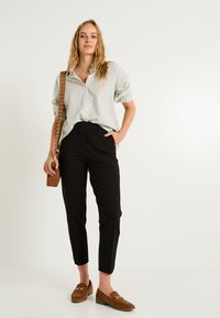 Camisa de botones a rayas en verde claro y blanco, pantalones negros ajustados, mocasines marrones y un bolso cruzado marrón con tachuelas.