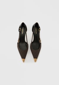 Smeđe cipele visoke potpetice šiljastog vrha s crnim kožnim remenčićem na peti i zlatnim detaljima. Imaju dizajn sa kopčom. Glatka tekstura.