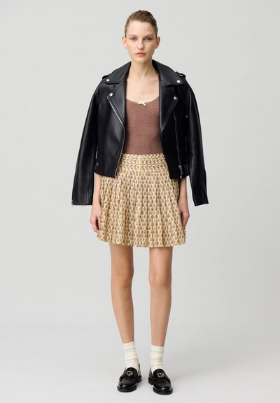 Chaqueta de biker de cuero negro sobre una camiseta sin mangas de canalé marrón, combinada con una falda plisada floral color crema, mocasines negros y calcetas color crema.