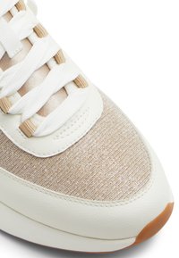 Sneaker med ovandel i vit läder och beige tyg, med en strukturerad yta och platta snören. Rund tå, gummisula med ljusbruna accenter.