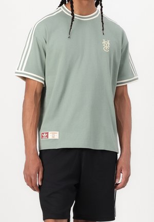 Jasnozielona koszulka z krótkim rękawem z białymi paskami, okrągłym dekoltem, logo marki na piersi oraz metką przy dołu. Dopasowana do czarnych szortów.