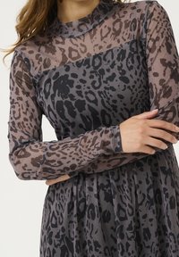 Robe transparente à manches longues, arborant un imprimé léopard gris et noir discret. Col haut, texture lisse et design de jupe plissée.