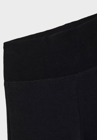 Ceinture élastique noire sur un vêtement en tissu doux, montrant un gros plan de la texture côtelée et des détails de couture lisse.