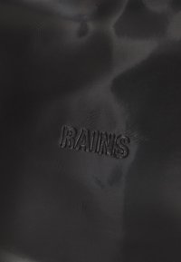 Črn vodoodporen material z rahlim leskom, s reliefnim logotipom "RAINS". Gladka tekstura z rahlimi površinskimi vzorci.