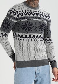 Pull gris avec motif bleu marine, comprenant des motifs géométriques et de flocons de neige, col rond et poignets côtelés.