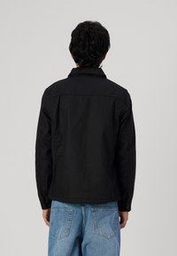 Svart, bomulljakke med krage og knappmansjetter, med rett snitt og glatt tekstur, sett fra baksiden, parret med lyseblå denim.