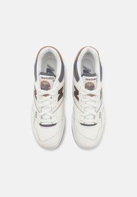 Valkoiset nahkakengät, joissa on harmaita ja ruskeita yksityiskohtia. Kengissä on pehmustettu nilkka, rei'itetty varvasosa sekä logo-yksityiskohtia sivuilla ja kielessä.