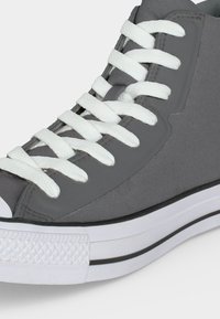 Γκρι sneaker ψηλού τύπου με λευκά κορδόνια και λαστιχένια σόλα με μαύρη ρίγα, εμφανίζεται από το πλάι κοντινή λήψη.