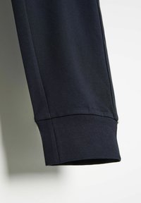 Granatowe bawełniane spodnie dresowe z tapered design, z prążkowanym mankietem i gładką teksturą. Widoczne detale na bocznych szwach.