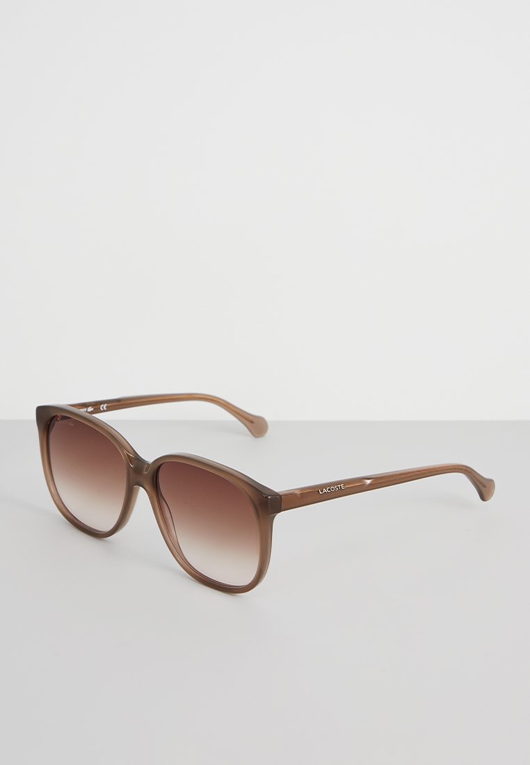 Lunettes de soleil marron surdimensionnées avec un verre dégradé, fabriquées en plastique léger. Présentent un design simple et un logo gravé sur la branche.