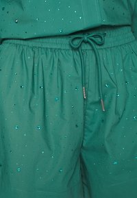 Pantalones cortos verdes hechos de una tela suave, con una cinturilla elástica, cordón y lentejuelas brillantes de color teal esparcidas.