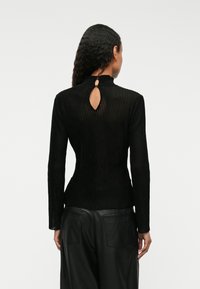 Musta ribattu pitkähihaine paita, jossa on korkea kaula-aukko, avainreikähäntä, sopiva siluetti ja teksturoitu kangas. Yhdistettynä nahkahousuihin.