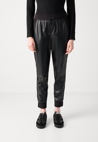 Black synthetic joggers with an elastic waistband and drawstring, featuring ribbed cuff details and a smooth sheen. Paired with black sneakers.