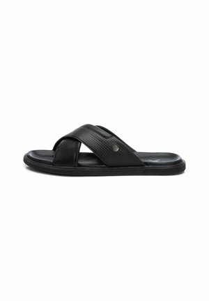 Sandalias negras sin hebilla con tiras cruzadas, parte superior texturizada, suela suave y sutil acento metálico. Diseñadas para la comodidad y facilidad de uso.