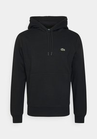 Sweat à capuche noir avec une poche kangourou, un cordon de serrage réglable, et un petit logo Lacoste vert sur la poitrine. Confectionné dans un matériau doux.