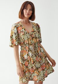 Floral dress featuring a V-neck, puff sleeves, and an elastic waist. Printed with vibrant orange, green, and white flowers on a brown background.
