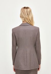 Dopasowana marynarka w brązowo-granatową kratę, posiadająca klapę, długie rękawy oraz zarysowany fason z detalem rozcięcia z tyłu.