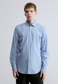 Helehall sinine pikkade varrukatega nööpidega särk, mis on valmistatud siledast kangast. Sellel on terav krae ja ümar alläär ning valged nööbid ees.