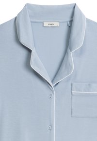 Jasnoniebieska bawełniana koszula piżamowa z kołnierzykiem z wycięciem, białym obszyciem i jedną kieszonką. Posiada zapięcie na guziki oraz miękką teksturę.