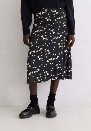 Black midi skirt with a floral print in light cream. Soft fabric, draped design, and a flowy silhouette. Paired with black socks and loafers.