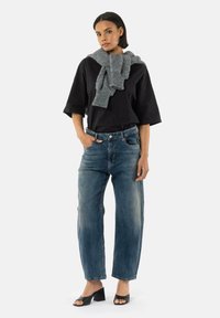 Haut noir oversize à manches courtes, jean droit en délavé moyen, écharpe en tricot grise, mules à talons ouverts noires sur un mannequin.