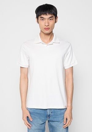 Polo blanco de manga corta con textura acanalada y cuello plano. Combinado con jeans de mezclilla azul claro, con un ajuste relajado.