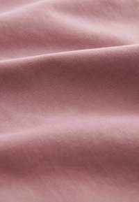 Tissu rose poudré doux et lisse avec un motif de tissage sergé diagonal et des plis délicats créant ombre et texture.