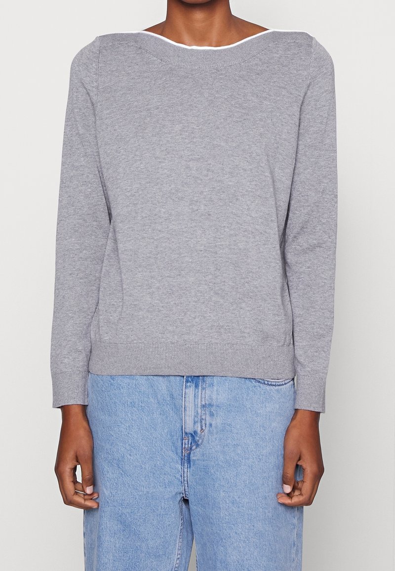 Grauer Strickpullover mit weitem Halsausschnitt, langen Ärmeln und geripptem Saum. Kombiniert mit hellblauen Jeans aus Denim mit lockerer Passform.