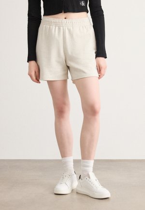 Lys beige shorts laget av mykt stoff med elastisk midje. Kombinert med hvite sneakers og en rillede svart langermet Cropped topp.