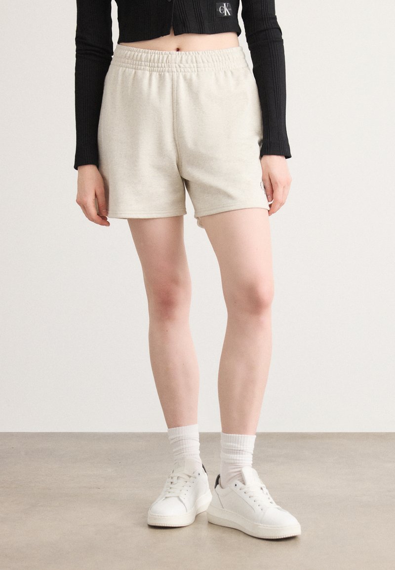 Lys beige shorts laget av mykt stoff med elastisk midje. Kombinert med hvite sneakers og en rillede svart langermet Cropped topp.