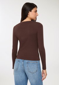 Brązowa bluzka z długim rękawem i okrągłym dekoltem, dopasowany krój, gładka faktura, zestawiona z jasnobłękitnymi dżinsami z wysokim stanem.